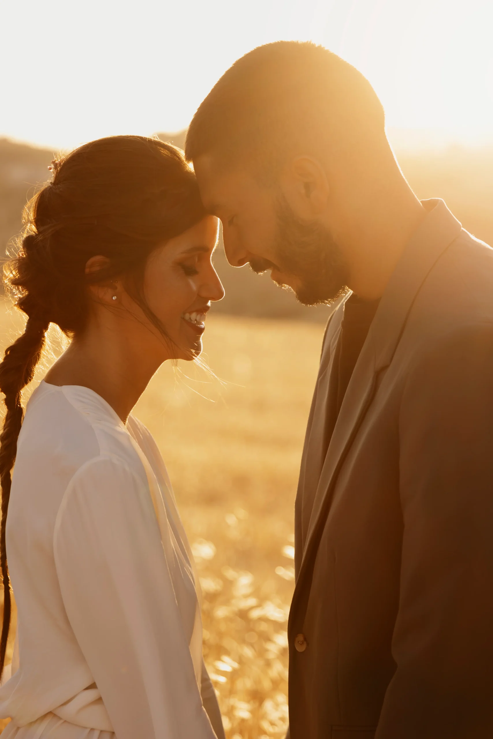 pareja de chico y chica tocándose la frente, con los ojos cerrados y en medio de un campo de trigo