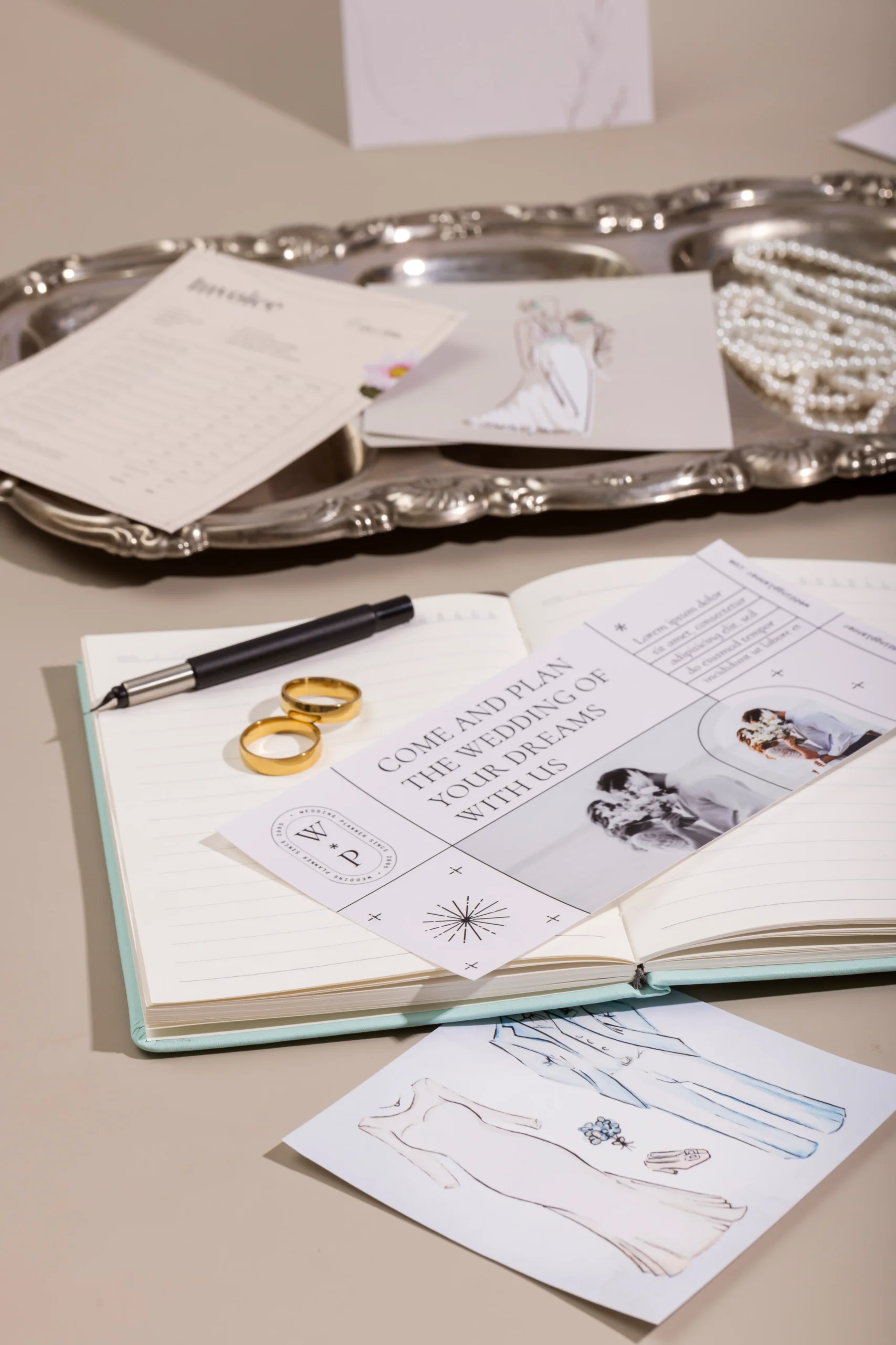 Mesa con varios objetos de decoración de boda sobre ella. Se ven unos anillos también sobre la mesa. Se están diseñando y verificando las ideas para la boda.